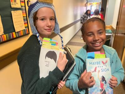 Two students hold annotated books up on their way to book club