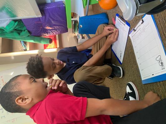 two boys work on a math problem with clip boards