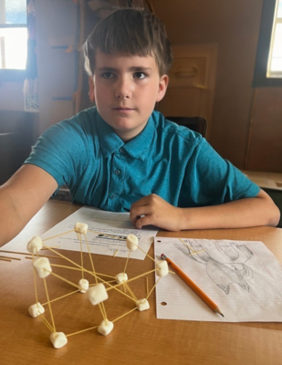 a boy shows off his model using pasta and marshmellows