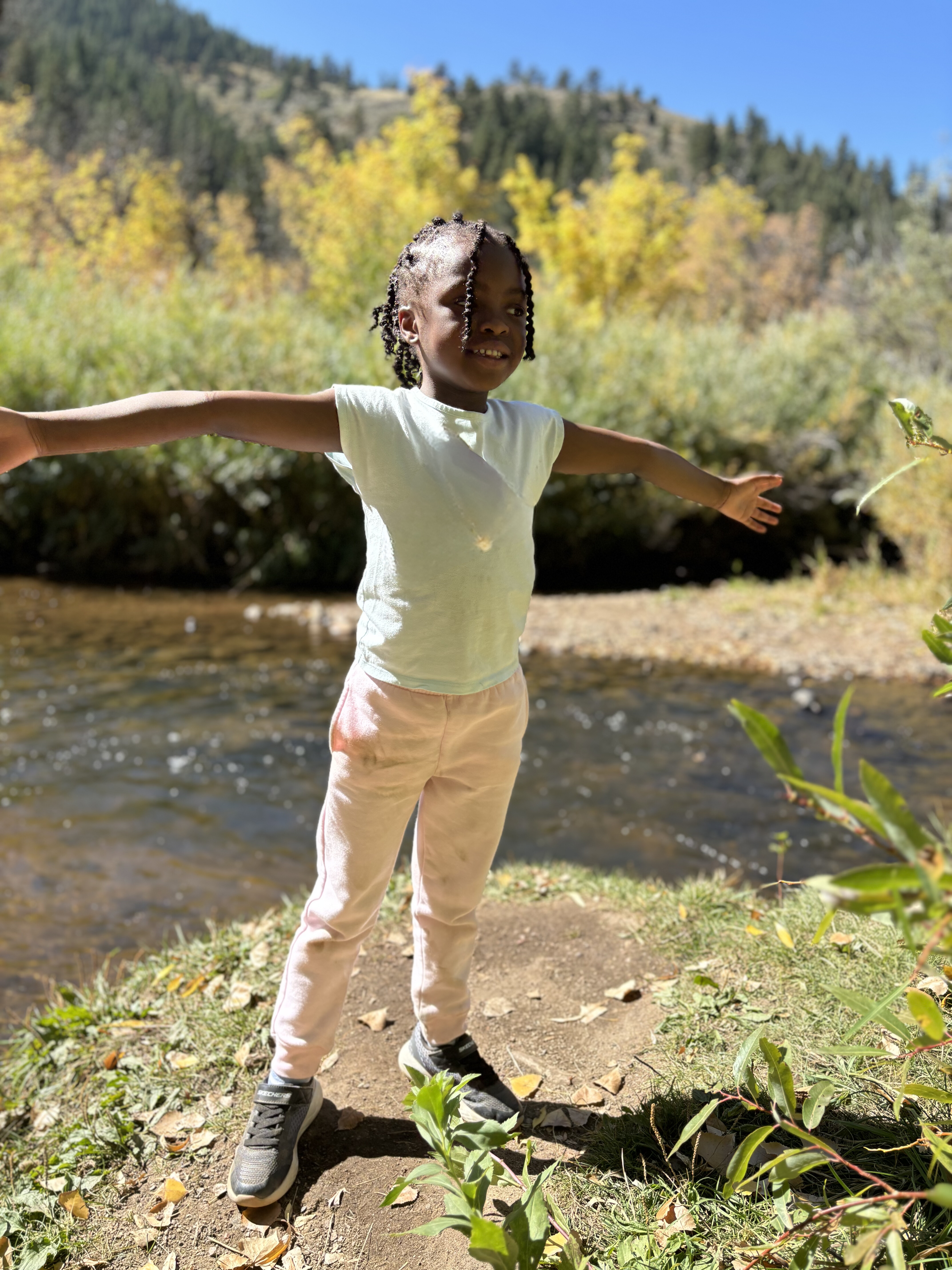 a young girl from St. Elizabeth's School stands by a mountain stream with arms open wide to the blue sky