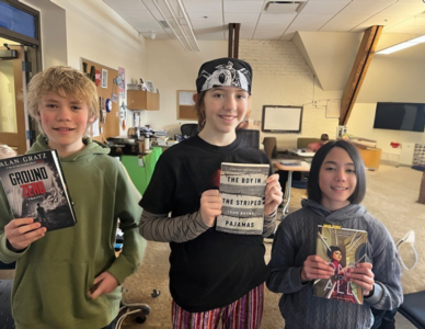 Three students hold up the books they are reading in middle school language arts