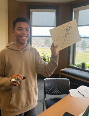 an 8th grade boy holds up a math problem on a white board